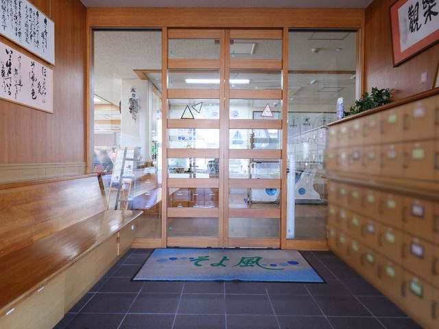 木製のエントランス風景 玄関 温かみのある木製のエントランス。患者様の名前入りの郵便ポストがあり、柔かな光が差し込む待合スペースが見えます。