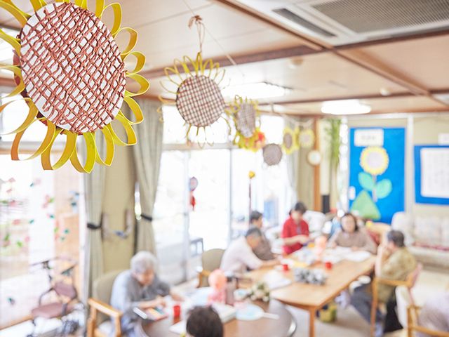 交流の場のリビング リビング 明るいリビングで、居住者がテーブルを囲み交流を楽しんでいます。飾り付けが施されています。