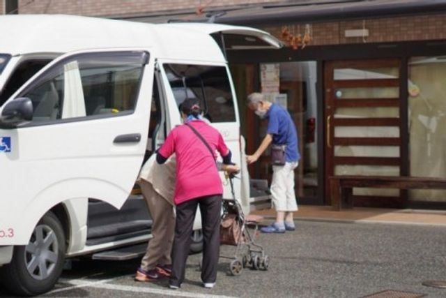 利用者の乗降風景 外観 職員が利用者を車からサポートする姿が見られます。通所者の安全な送迎を行っています。