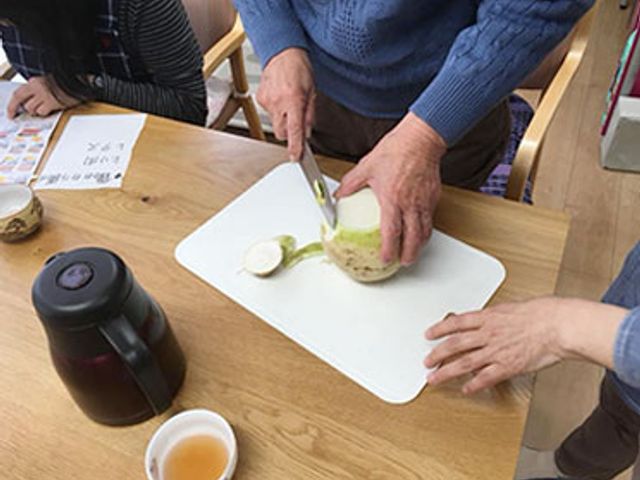 テーブルで人が大根を切る様子 キッチン 調理活動を通じて、利用者同士のコミュニケーションが深まる場です。