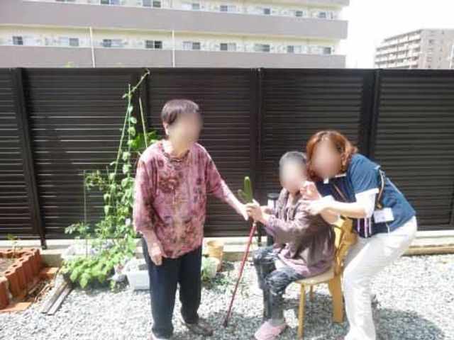 園芸活動の応援風景 イベント 利用者の園芸活動をスタッフが優しく支援している光景です。手入れされた中庭で心地よい時間を過ごせる環境が整っています。