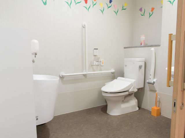 手すり付きのトイレ トイレ 手すりを設置した清潔で使いやすいトイレが整っており、安心してご利用いただけます。壁にはカラフルな装飾も施され、温かみのある空間を演出しています。