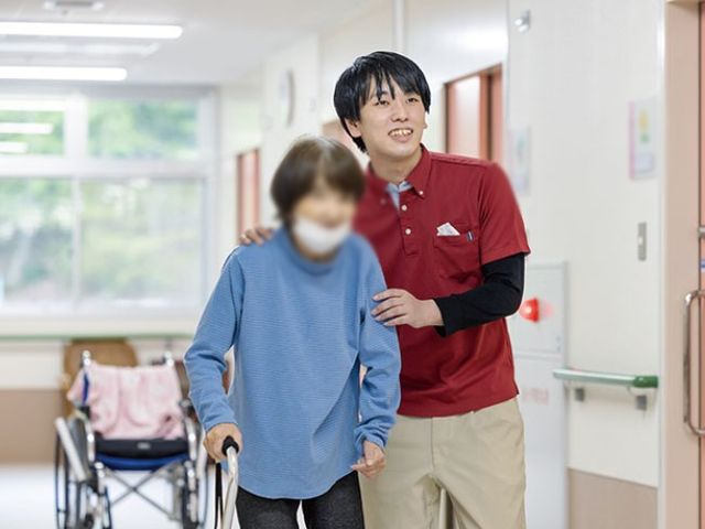 歩行をサポートする様子の廊下 廊下 明るい廊下で親切なスタッフが利用者の歩行をサポートしています。安心して移動できる環境が整っています。