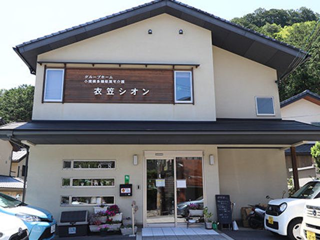 木の看板がかかる外観 外観 自然に囲まれた立地で、穏やかな環境が魅力です。建物正面には温かい雰囲気の木製看板があります。