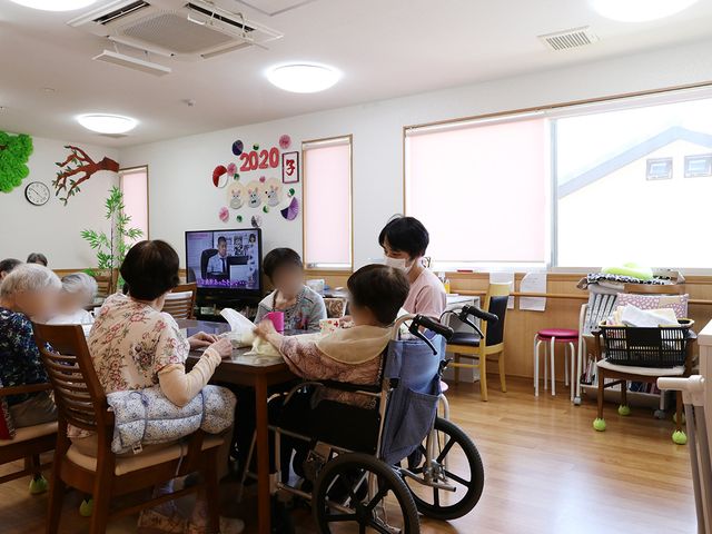 車椅子利用者の居室 居室 明るい空間で、車椅子の利用者も参加可能なテーブルが設置されています。テレビを見ながら歓談している様子です。