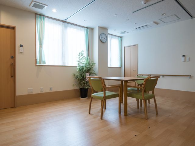 明るい居室のテーブルと椅子 共有スペース 清潔感のあふれる居室には、木目調の床と窓からの自然光が、温かな雰囲気を醸し出しています。お仕事で利用される方にも穏やかな時間を提供できる空間です。