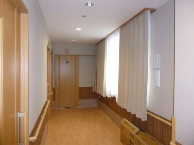 清潔な廊下の様子 通路 明るい木目調の廊下が見受けられ、天井の照明も十分な明るさを提供しています。通路は広く、清潔感のある空間です。