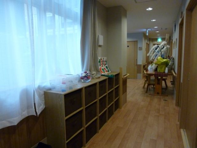 明るい廊下の風景 通路 清潔感のある廊下は、居心地の良さを感じさせます。奥には職員が利用者様のサポートをしている様子が見受けられます。