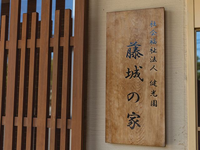 看板の施設名 看板 入り口横の看板が、施設の名前をしっかりと示しています。温かみのある木のデザインです。