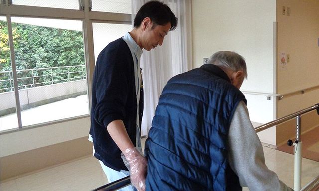 スタッフが手助けする廊下 廊下 自然光が差し込む明るい廊下で、スタッフがしっかりと利用者をサポートしています。