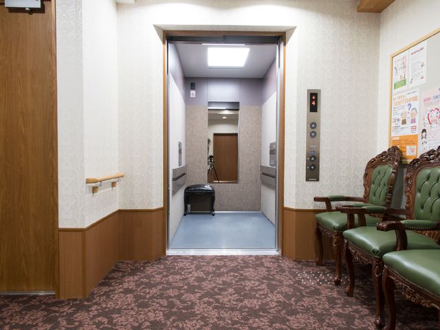待合エリアのエレベーター前 エレベーター前 座り心地のよい椅子が並ぶ待合エリアです。利用者さまが快適にお待ちいただけるように工夫されています。