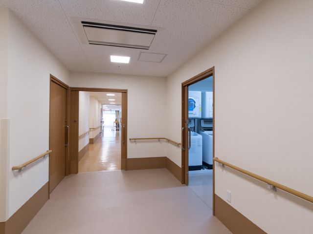 明るく清潔な廊下 ランドリールーム 手すりが整備された安全な通路です。遠くには複数の方が快適な移動をされています。