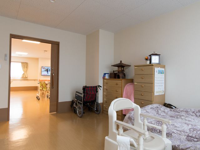 居室と廊下の様子 居室 広々とした居室には、必要な家具が整っており、廊下には歩行器も見えます。個々の生活スタイルが尊重された環境です。
