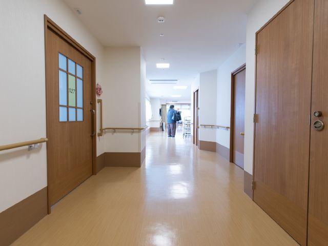 廊下に2人と歩行器 廊下 手すりがある明朗な通路です。訪れる方々が安心して歩けるよう、歩行器を使ったケアも行われています。