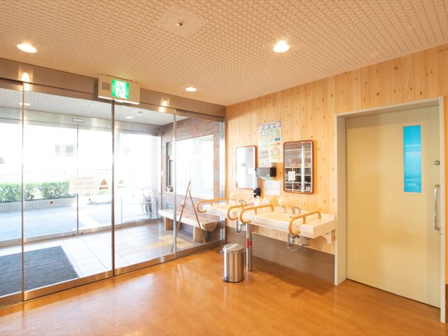 入口の明るいエントランス エントランス 明るい雰囲気のエントランスで、壁には木材を使用して暖かみのある設計です。手洗い場も完備され、衛生的な環境が保たれています。