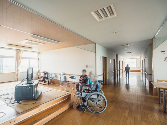 明るい共有スペースの廊下 リビング ゆとりのある廊下には、椅子が並び、車椅子を利用する方が一息ついていらっしゃいます。窓から入る自然光が心地よい空間を演出しております。
