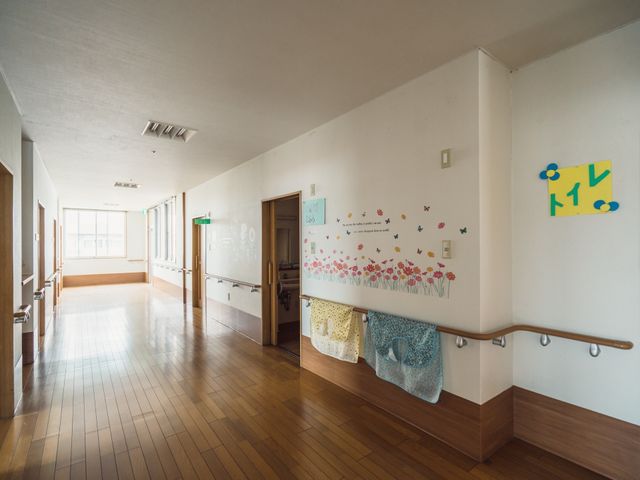 明るい廊下と掲示物 廊下 広々とした廊下には、手すりと壁面装飾が施されており、温かみのある雰囲気です。来訪者と利用者の心を和ませる空間作りがされています。