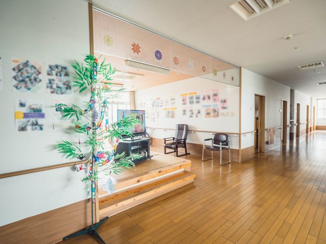 廊下に飾り付け掲示物 リビング 広々とした明るい廊下には、壁に色とりどりの掲示物が飾られ、温もりのある雰囲気が漂っています。ゆったりと配置された椅子も、休憩に適しています。