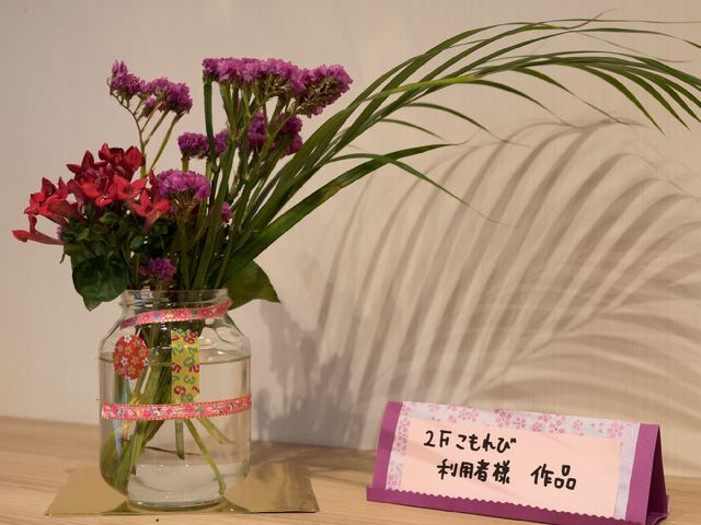 花瓶と案内表示の写真 施設利用者の作品 優しい色合いの花がロビーを明るく彩り、訪れる方々を温かく迎え入れます。手作り感のあふれる案内も素敵なアクセントです。