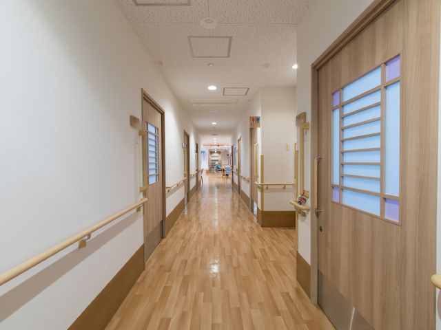 温もりある廊下の様子 廊下 すり足で歩かれる方々を支える手すりが設けられた廊下です。木目調の壁が温かみを感じさせ、心地よい空間を提供しています。