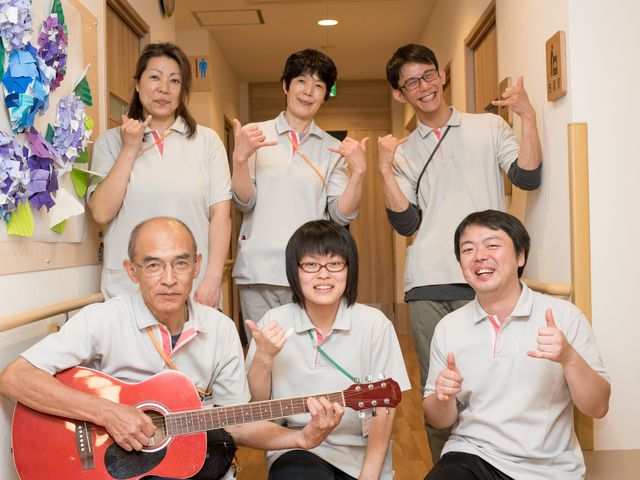 スタッフの笑顔とギター 明るい職員 ご利用者様に寄り添う温かい人材が集うチームワークです。音楽を通じて楽しい時間を提供しています。