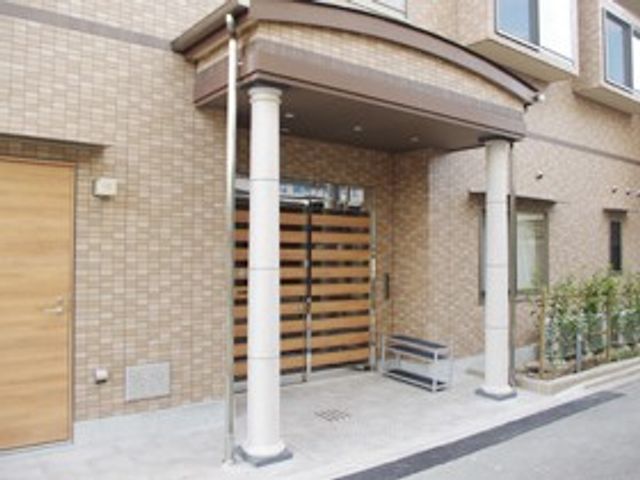 建物の出入口 外観   落ち着いた色合いの建物前に、柱のある出入口が見えます。植栽もあり、やわらかな雰囲気です。