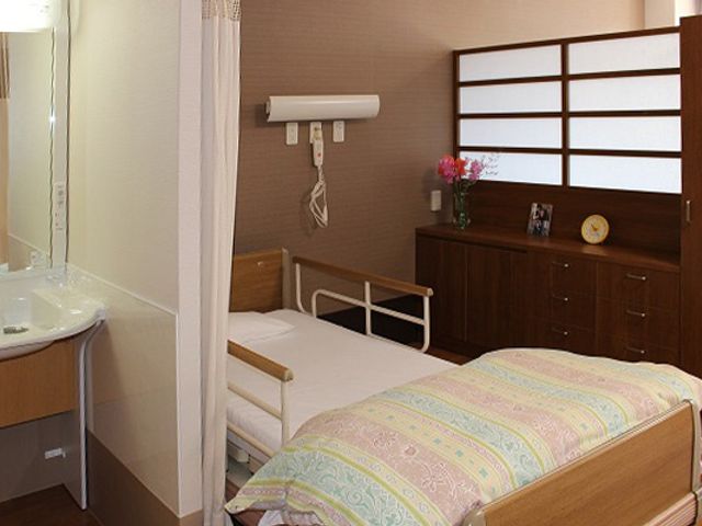 ゆったりした個室の居室 居室 広々とした居室は、安心して快適な日々を過ごすための設計が施されています。白と木目調の落ち着いた色合いで、家庭の温かみを感じさせます。