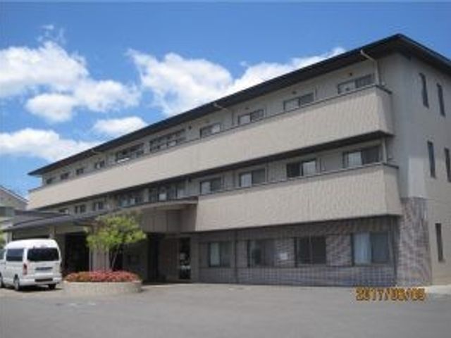 建物外観 外観   3階建ての落ち着いた色合いの建物です。青空の下にあり、入口まわりに植栽も見えます。