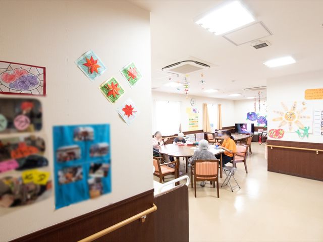活動スペースの様子 談話室 明るく広々とした食堂で、ご利用者が集い楽しく会話を交わしています。壁には手作りの飾りがあり、温かみのある雰囲気が漂います。