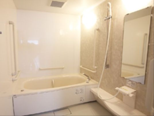 広々とした浴室の中に、浴槽とシャワーが完備されている。浴槽近辺と内部に手すりが設置されている。大きな鏡がある。