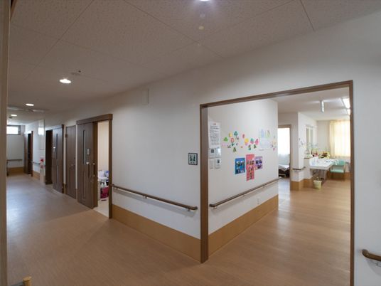 白を基調とした清潔感のある幅の広い廊下で、壁には手すりが設置されている。共有スペースの入り口が開放されている。