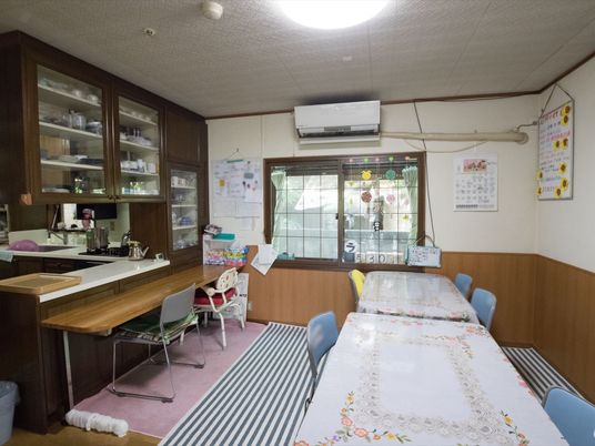 大きな棚の中にたくさんの食器が収納されており、キッチンの前には長机が置かれている。壁にホワイトボードが掛けられている。