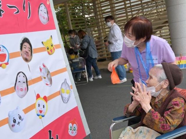 祭りを楽しむ屋外の様子 中庭   屋外で催しを楽しむ様子が見えます。車椅子の方にスタッフが寄り添い、和やかな雰囲気が伝わります。