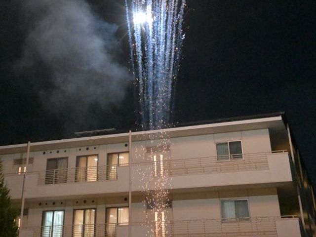 花火を見上げる外観 外観   夜空に打ち上がる花火を、建物前の皆さんが見上げています。にぎやかな催しが行われている様子が伝わります。