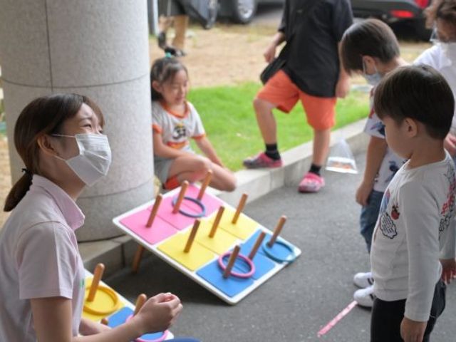 子どもと遊ぶスタッフ 外観   屋外で子どもたちと輪投げを楽しむスタッフの様子です。明るい交流の場がある雰囲気が伝わります。