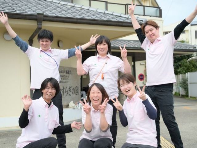 スタッフ集合の外観前 外観   施設の前でスタッフの皆さんが笑顔でポーズを取っています。明るい雰囲気で、働く人の元気さが伝わります。