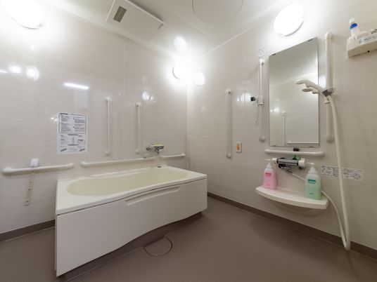 明るい照明と広々とした空間の個室タイプの浴室である。浴槽やシャワーの周辺には、たくさんの手すりが設置してある。