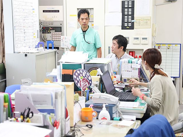 活気あるオフィス内観 スタッフイメージ スタッフがデスクで活発に話し合いをしている様子です。コミュニケーションが盛んな職場環境です。