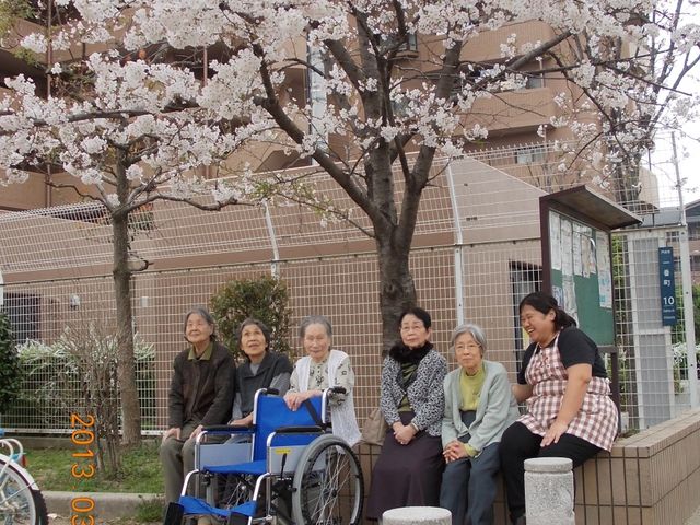 桜の木と共に笑顔の集い イベント 桜の木の下、和やかに話しながら過ごす人々の姿が、快適なコミュニティの一コマを映し出しています。ゆったりとした時間が流れる中庭で、心豊かな日々を想像してみてください。