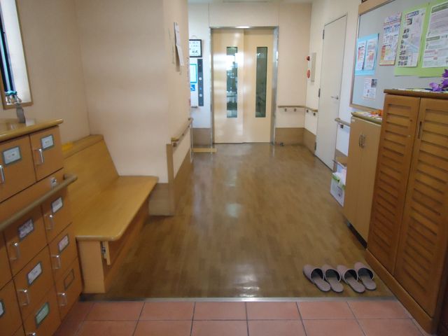 廊下の清潔な様子 玄関 広々とした廊下はきれいに保たれており、来訪者を迎えるベンチも設置されている安心の空間です。靴が並べられた玄関付近は社会とつながる暖かい出迎えの場となっています。