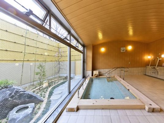 大浴場内の右側にはシャワーや蛇口が設置され、左側には木材で縁取られた浴槽が設置されている。まどの外は庭園のような装飾が施されている。