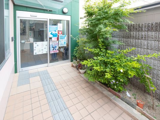 施設の玄関は自動ドアである。ガラス面にはさまざまなポスターが掲示されている。玄関前には植栽があり、緑豊かな空間である。