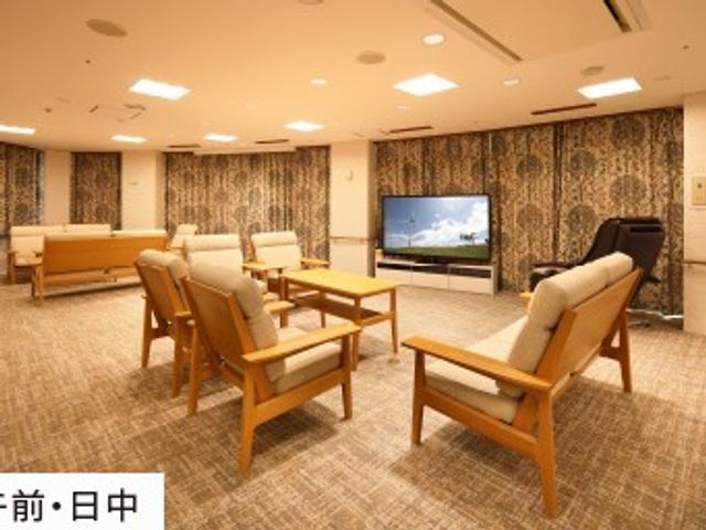 明るい共用ラウンジ ラウンジ   広いスペースに木製の椅子とテーブルが並ぶ、落ち着いた雰囲気の共用ラウンジです。テレビもあり、くつろぎや会話の時間を過ごしやすそうです。