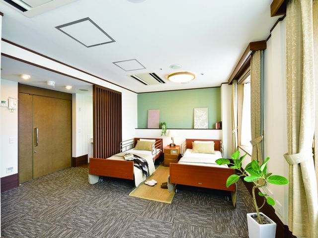 居心地の良い洋室 夫婦部屋 落ち着いた色合いのベッド周り、日中の優しい光が差し込む空間です。