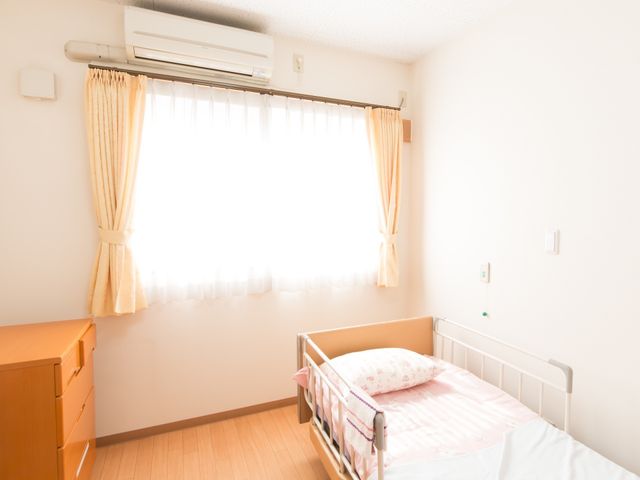 明るい個室のベッド 居室 ゆとりを持つ個人の空間で、ベッドサイドには日常生活に必要な家具も完備。安心して過ごせる環境をご提供します。