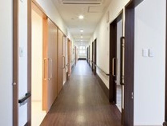 廊下はフローリングの床で居室ドアが等間隔に並んでいる。壁には手すりが取り付けられ、移動の補助としてご利用いただいている。