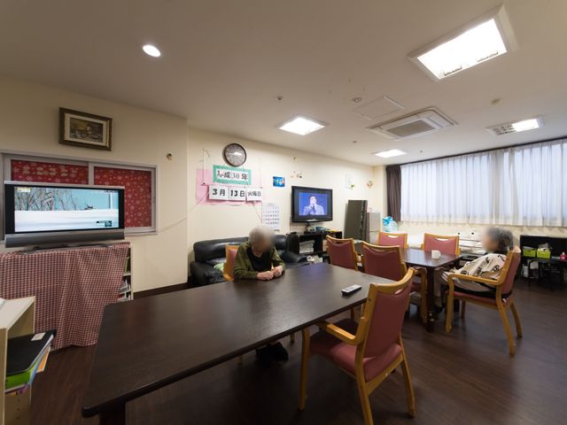 共有リビングエリア 食堂 ソファとテーブルが配置された快適な共有リビングで、テレビを視聴しながらゆったりとした時間を過ごしている方がいらっしゃいます。