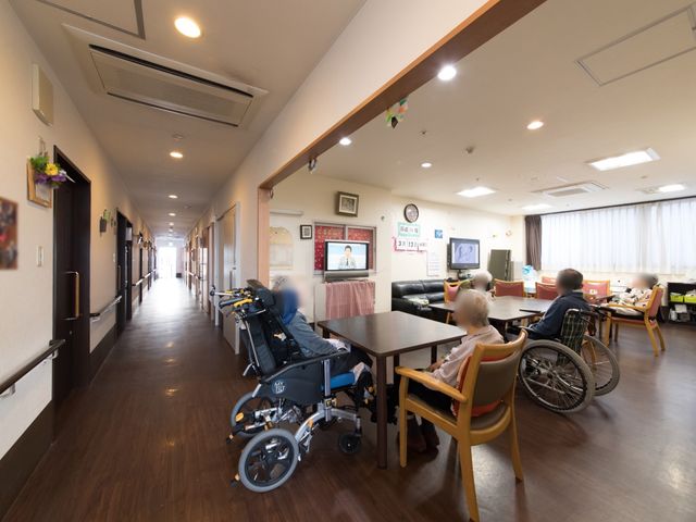 共有スペースの明るい様子 食堂 ゆったりとしたラウンジでは、皆さんがテレビを視聴されている心和む光景です。椅子に座る方々のリラックスした姿が印象的です。