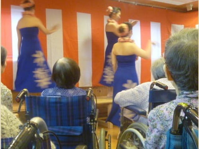 演技鑑賞の住人たち 多目的室 華やかな演技を楽しむ住人たちが椅子に座って集まる、温かい交流の場です。