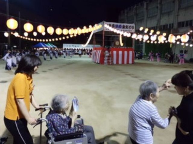 盆踊りが行われる広場 祭り 提灯で彩られた中庭で、利用者の皆さまが盆踊りを楽しまれています。一緒に心躍る時間を過ごすことができる空間です。